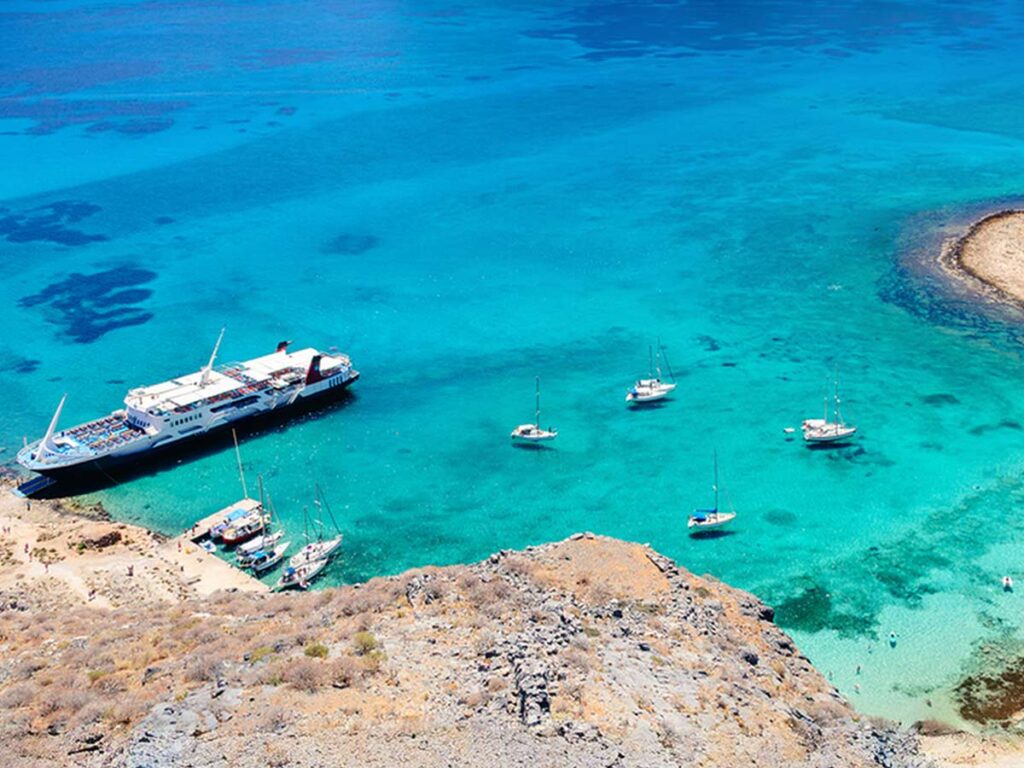 Aerial view of cruise ships and yachts docked in the turquoise waters of Gramvousa Island, Crete – a popular cruise stop.