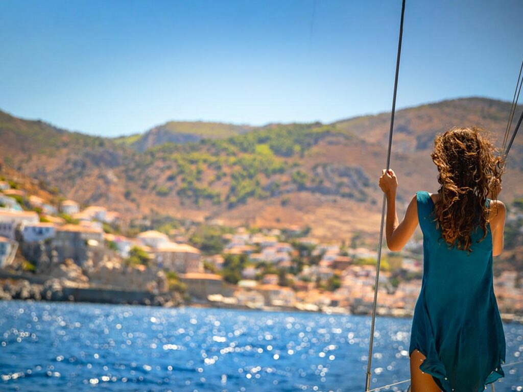 Woman standing on a sailing boat, enjoying the coastal view of a Cretan town during a private cruise – ideal for luxury sea travel in Crete.
