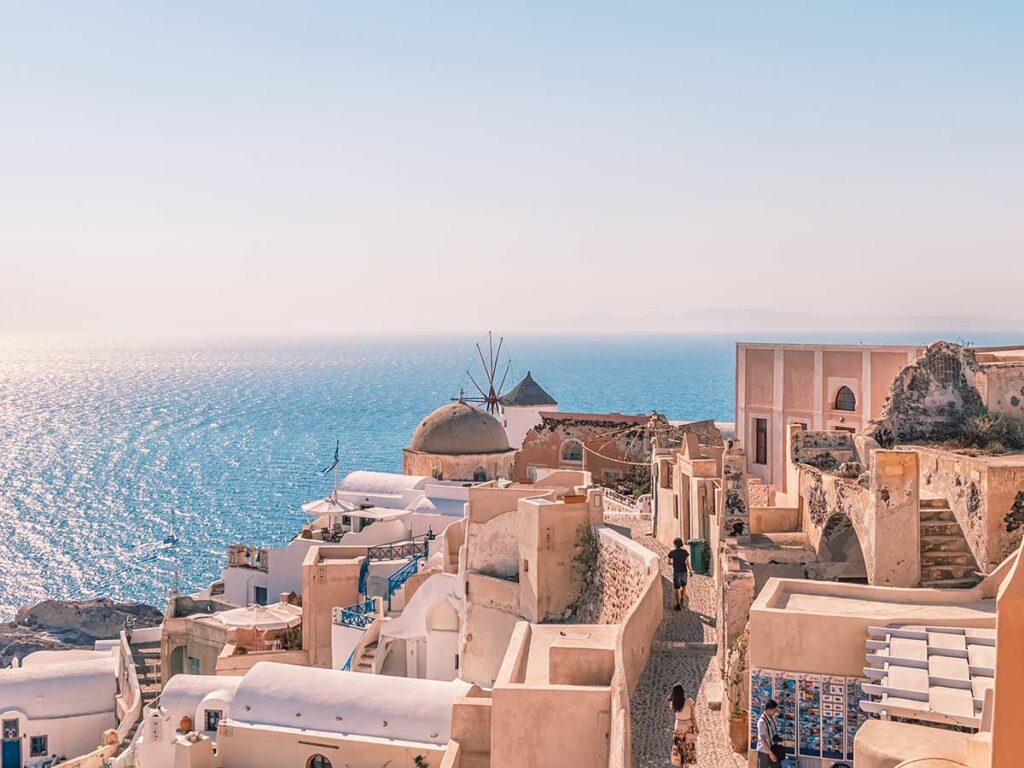 Walkway in Oia with windmill, domed houses and Aegean Sea views under bright sunlight