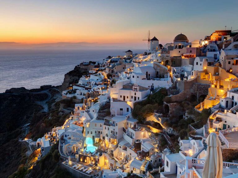 Sunset view of Oia with illuminated Cycladic houses and sea in the background