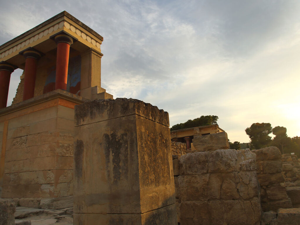 <strong>Crete temperature by month: What to expect all year round</strong> 2 Sunset view of the Palace of Knossos in Crete, featuring iconic red Minoan columns and ancient ruins from the Minoan civilization.