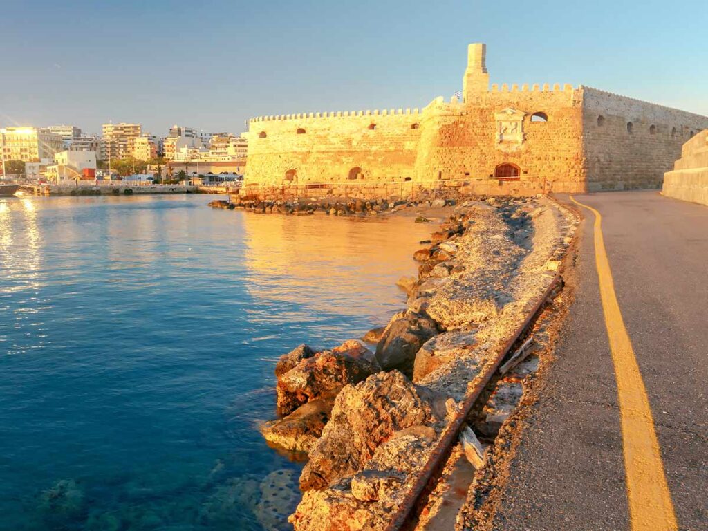 <strong>Planning your Knossos Palace tour: Must-see highlights and tips</strong> 5 The stone walls of the Koules fortress bathed in golden sunlight next to the sea of Heraklion.