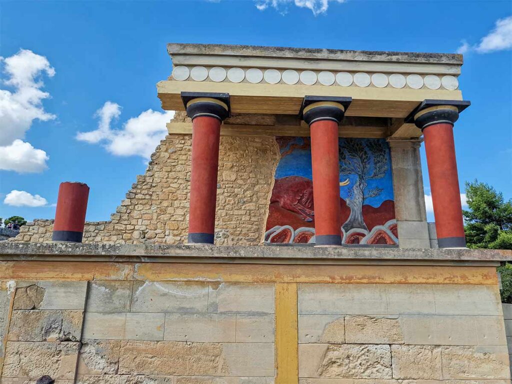 <strong>Planning your Knossos Palace tour: Must-see highlights and tips</strong> 2 The famous Minoan fresco featuring a relief bull and an olive tree between the red columns at the Palace of Knossos.